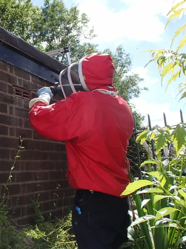 About SwarmCatcher 1 Beekeeper in a red bee suit removing honey bees from an air brick in a house wall at Abercynon